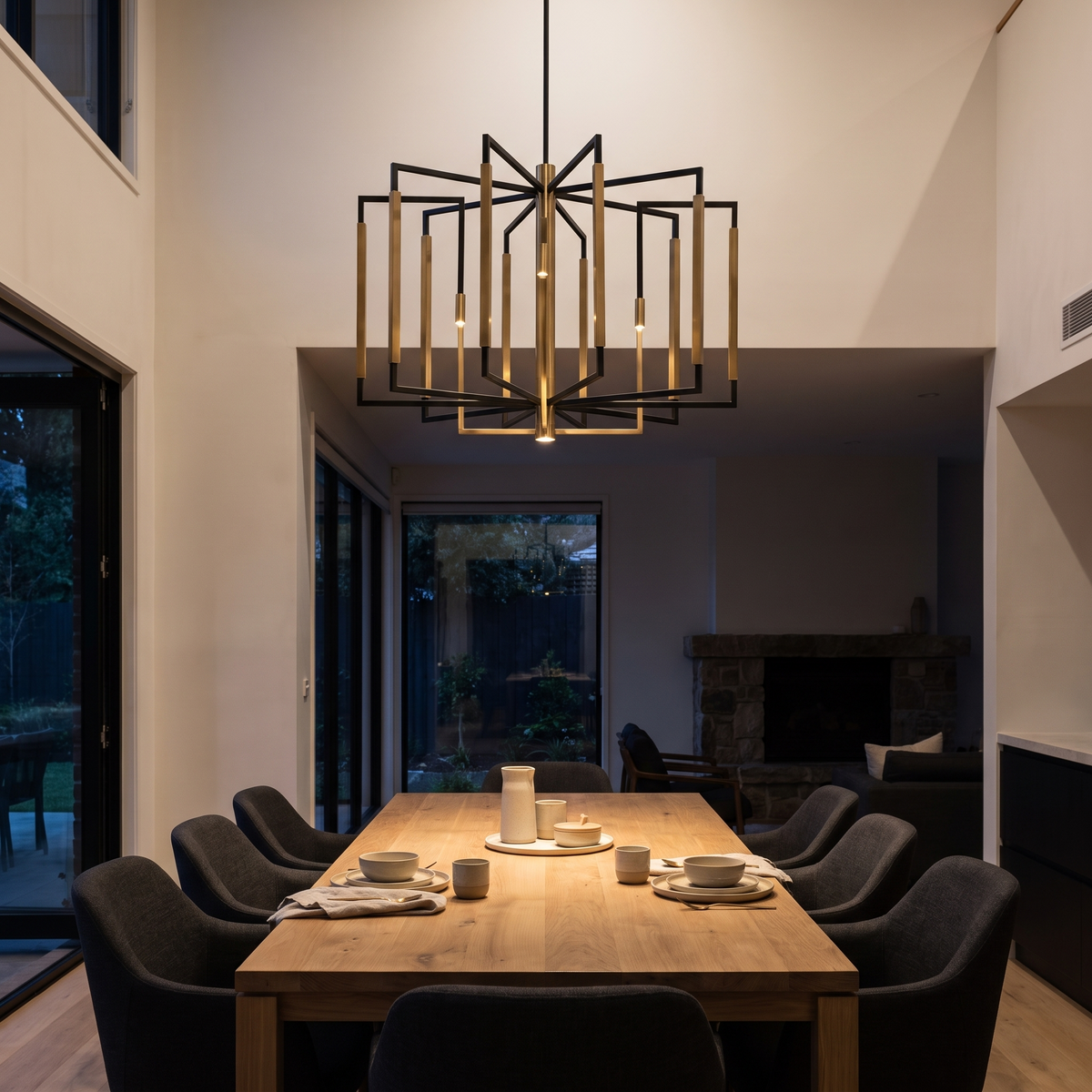 Dining room at night lit by a black and brass geometric ceiling fixture